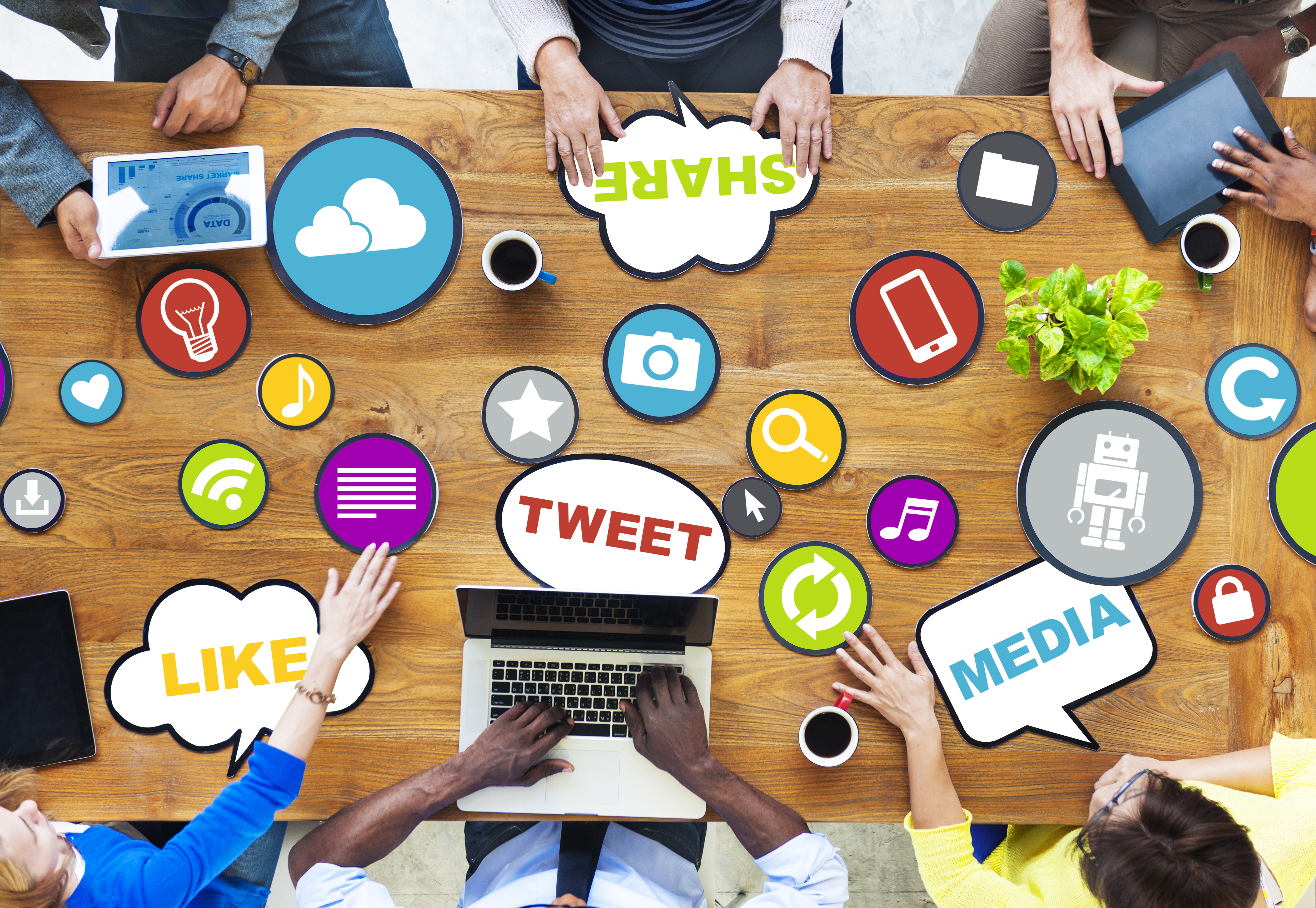 hands of people sitting around table with tablets and a laptop computer, coffee, and several generic social media graphics